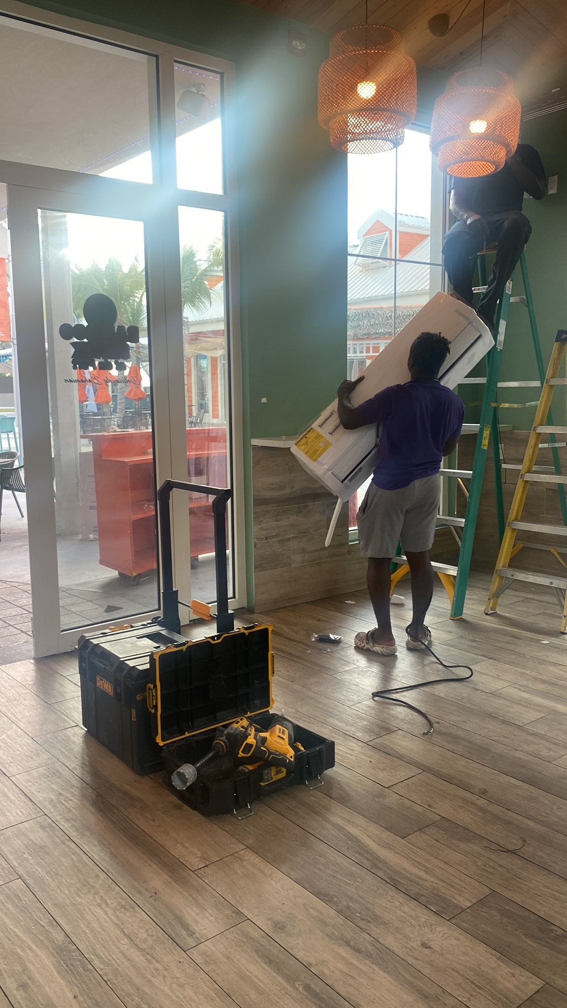 Two-man team mounting indoor AC unit in a restaurant with ladders